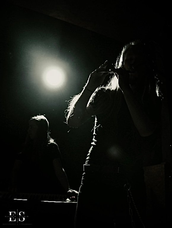 Musician playing a tin whistle in silhouette beneath a bright stage light